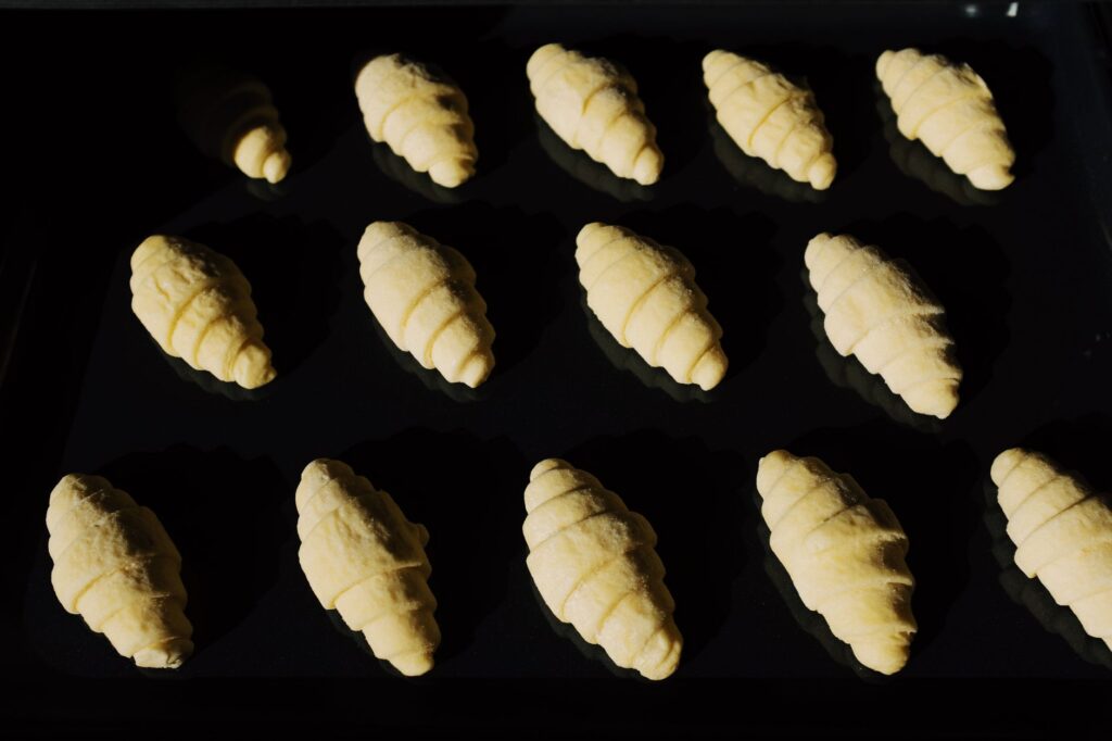 Croissante aurii proaspăt scoase din cuptor, așezate pe o tavă cu hârtie de copt