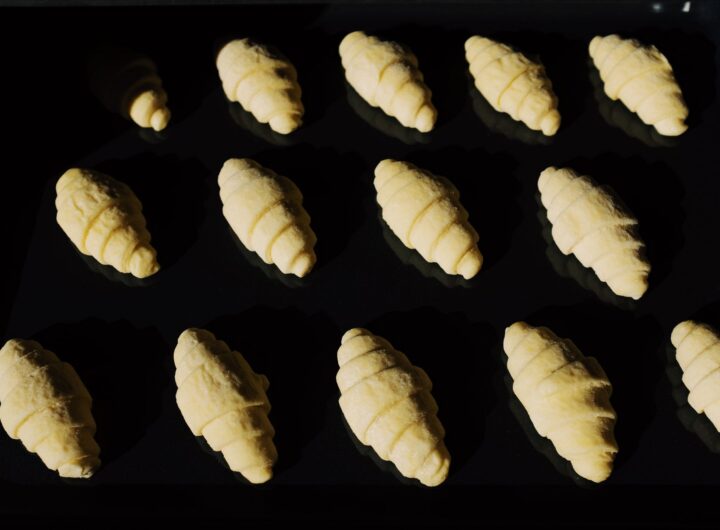 Croissante aurii proaspăt scoase din cuptor, așezate pe o tavă cu hârtie de copt