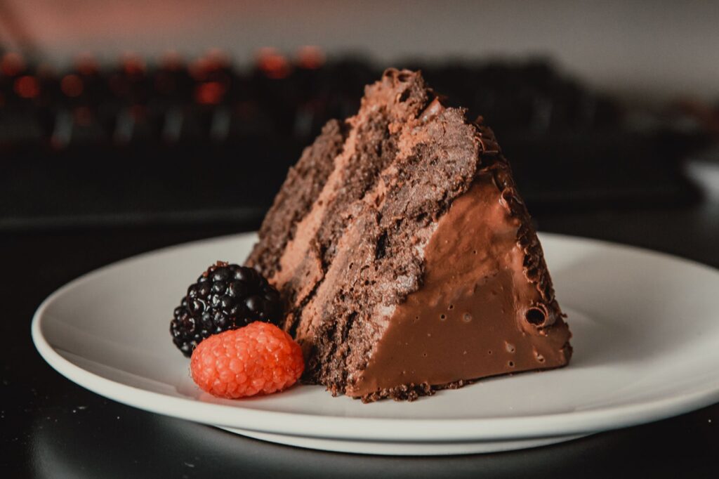 Felie de tort de ciocolată cu straturi de blat de cacao și cremă, acoperită cu glazură lucioasă